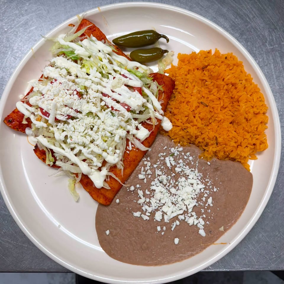 Mexican plate with enchiladas topped with lettuce, cream, and cheese, served with orange rice, refried beans, and jalapeños.