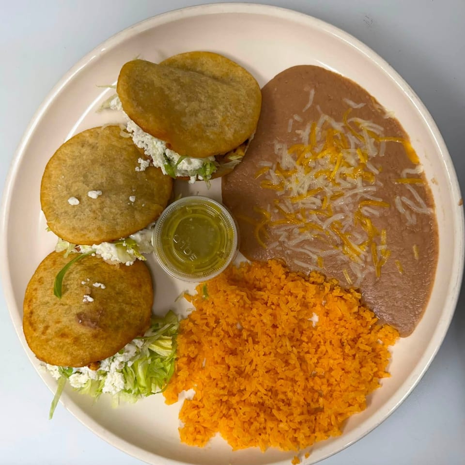 Mexican plate with crispy tacos, enchiladas topped with cheese and onions, orange rice, salad, and green salsa.